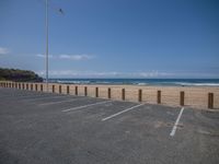 an empty parking lot on the beach next to the ocean by some tall poles and poles