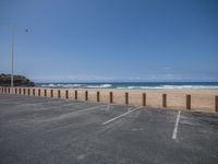 an empty parking lot on the beach next to the ocean by some tall poles and poles