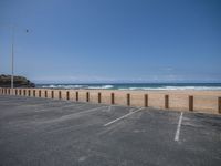 an empty parking lot on the beach next to the ocean by some tall poles and poles