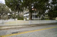 there is a white fence next to the house with a white picketer fence and a street in front