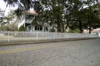 there is a white fence next to the house with a white picketer fence and a street in front