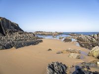 a beautiful beach with large rocks in it and water running along the sand under it