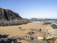 a beautiful beach with large rocks in it and water running along the sand under it