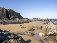 a beautiful beach with large rocks in it and water running along the sand under it