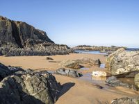 a beautiful beach with large rocks in it and water running along the sand under it