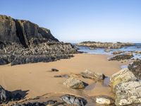 a beautiful beach with large rocks in it and water running along the sand under it