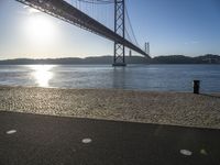 sun shines near the water and bridge over the water on a sunny day, with a sand beach next to it