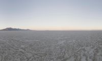 a beautiful view of some very small mountains in the distance is an icy body of water and a large snow field