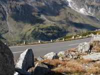 a mountain road is lined with boulders and rocks next to a mountain range with tall, grassy hills in the distance