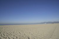 people walk on sand at a beach, near the ocean in the distance is a sky with few cloudless, and blue skies