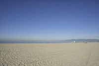 people walk on sand at a beach, near the ocean in the distance is a sky with few cloudless, and blue skies