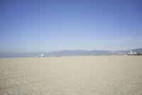 people walk on sand at a beach, near the ocean in the distance is a sky with few cloudless, and blue skies