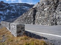 a stone wall on the side of a road in front of a snowy mountain,