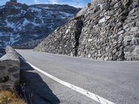 a stone wall on the side of a road in front of a snowy mountain,