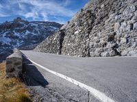 a stone wall on the side of a road in front of a snowy mountain,