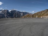 a person on a skateboard stands in an empty parking lot surrounded by snowy mountains