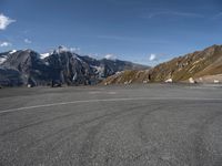 a person on a skateboard stands in an empty parking lot surrounded by snowy mountains