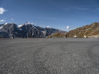 a person on a skateboard stands in an empty parking lot surrounded by snowy mountains