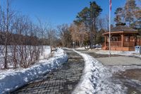 a walkway surrounded by snow next to a small gazebo on a clear day with blue skies