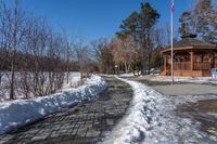 a walkway surrounded by snow next to a small gazebo on a clear day with blue skies