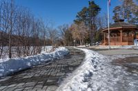 a walkway surrounded by snow next to a small gazebo on a clear day with blue skies