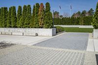 a view of a park with some stone walkways and bushes in the background with flags flying behind a statue