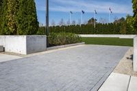 a view of a park with some stone walkways and bushes in the background with flags flying behind a statue
