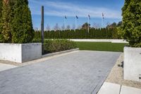 a view of a park with some stone walkways and bushes in the background with flags flying behind a statue