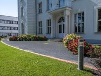 a tall building with a white picketer and walkway through it and many potted flowers on the lawn