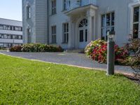 a tall building with a white picketer and walkway through it and many potted flowers on the lawn