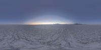 a view of the sun rising over a barren plain with snow all around it and mountains in the distance