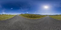 360 - camera image of road in grassy area and a mountain view in distance, looking straight ahead