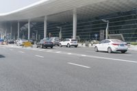traffic moves past the front of an airport terminal where there is only one passenger on the bus