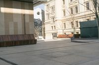 a sidewalk in a town that has benches on both sides of it with buildings in the background