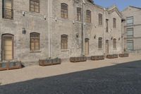 the person is walking down the street near old buildings on a sunny day with a red umbrella