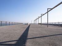 a bench near the ocean on a sunny day, with shadows of benches and poles