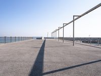 a bench near the ocean on a sunny day, with shadows of benches and poles