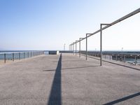 a bench near the ocean on a sunny day, with shadows of benches and poles