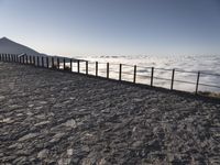 a bench that is on top of a stone area next to the ocean and a large mountain in the distance