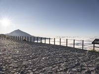 a bench that is on top of a stone area next to the ocean and a large mountain in the distance