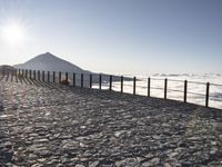 a bench that is on top of a stone area next to the ocean and a large mountain in the distance