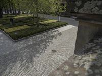 two benches sitting outside on the side of a sidewalk next to a building with a brick walkway that looks out over a formal garden