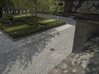 two benches sitting outside on the side of a sidewalk next to a building with a brick walkway that looks out over a formal garden