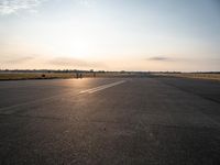 a small airplane is taking off in a wide open field, and the sun sets on the runway