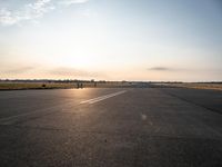 a small airplane is taking off in a wide open field, and the sun sets on the runway