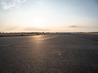 a small airplane is taking off in a wide open field, and the sun sets on the runway