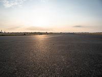 a small airplane is taking off in a wide open field, and the sun sets on the runway