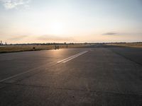 a small airplane is taking off in a wide open field, and the sun sets on the runway