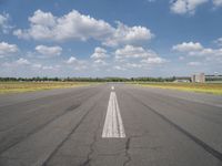 an empty runway surrounded by a field and blue sky with fluffy clouds in the background