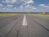 an empty runway surrounded by a field and blue sky with fluffy clouds in the background